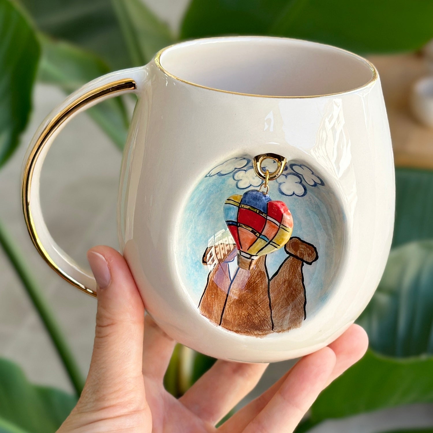 Ceramic mug with gold handle and balloon-dog artwork, held in a hand