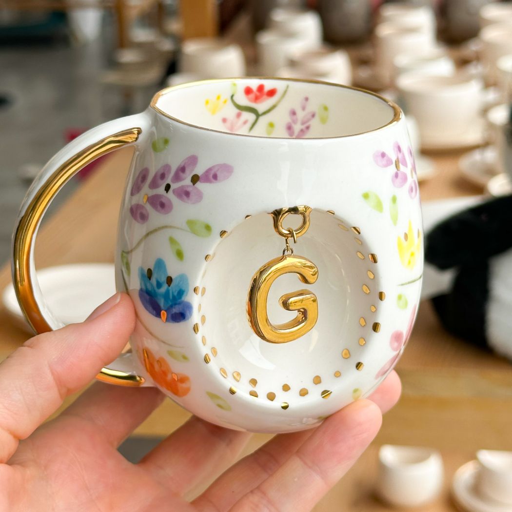 Porcelain mug with gold handle, floral pattern, and raised gold letter G on the front