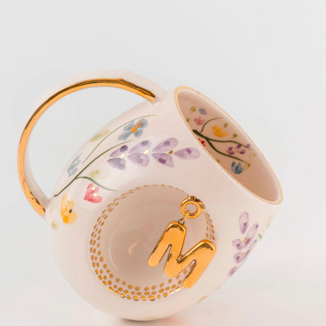 Porcelain mug with gold handle, floral pattern, and raised gold letter K in circular design