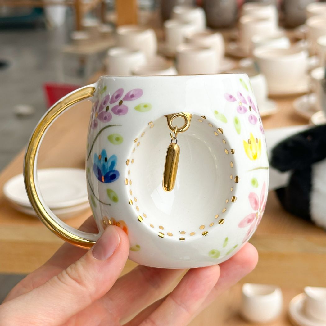 Porcelain mug with gold handle, floral pattern, and raised gold letter I on the front