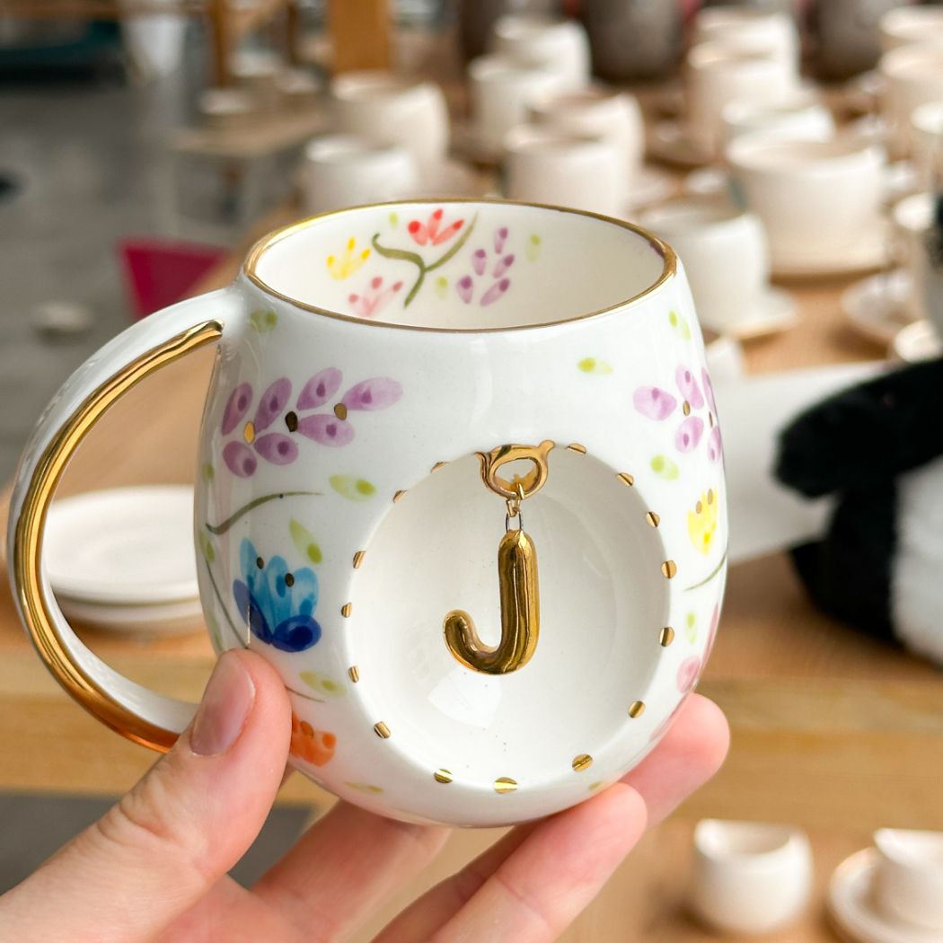 Porcelain mug with gold handle, floral pattern, and raised gold letter J on the front