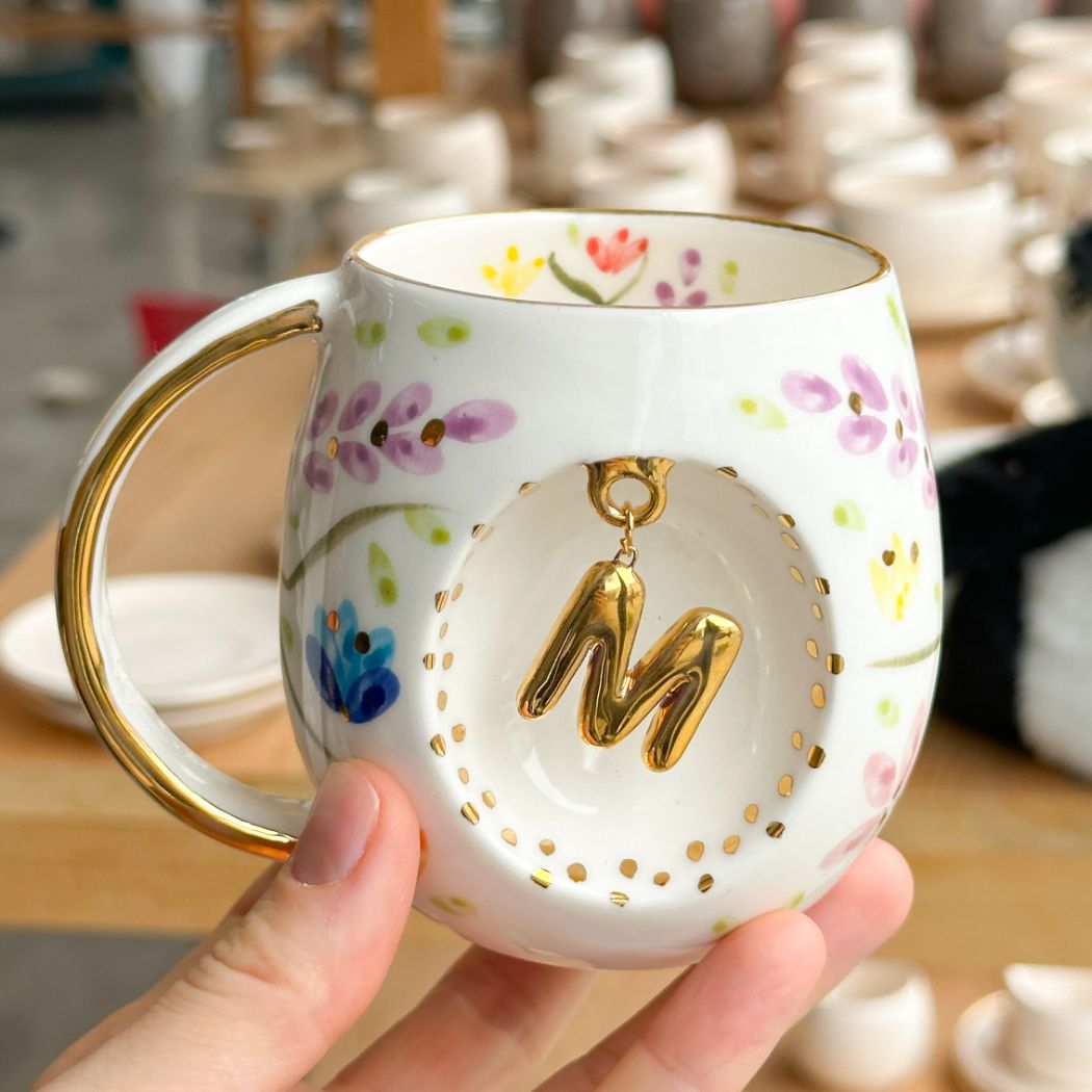 Porcelain mug with gold handle, floral pattern, and raised gold letter N on the front