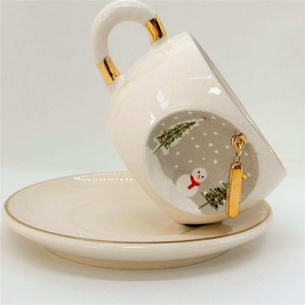 Porcelain tea cup with saucer, gold handle accents, winter letter charm and snowman detail