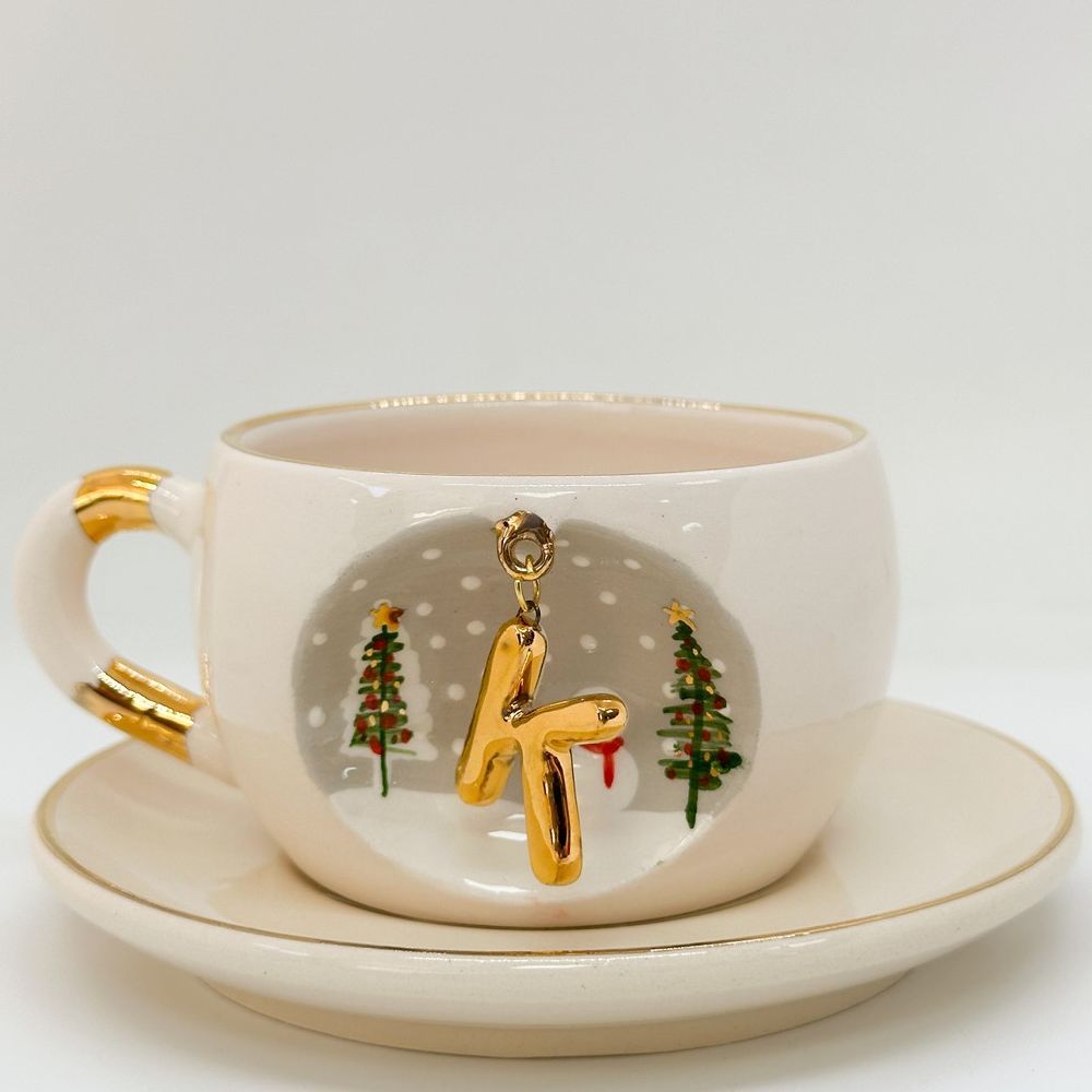 Porcelain tea cup with saucer, gold handle and hanging winter letter charm with trees and snowman