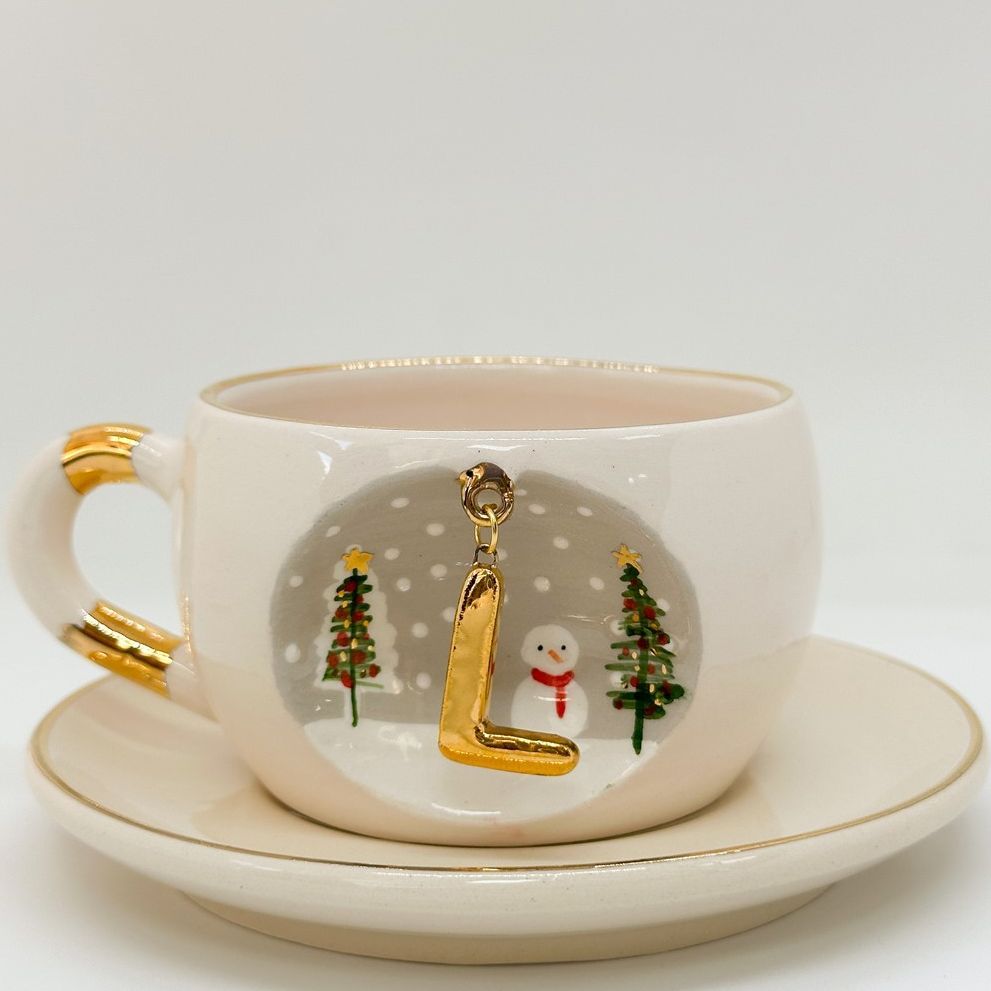 Porcelain tea cup with saucer, gold handle, hanging winter letter charm with Christmas trees and snowman