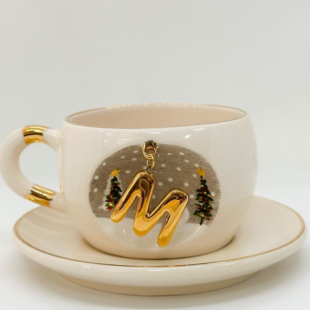 Porcelain tea cup with saucer, gold handle and winter letter charm with Christmas trees illustration