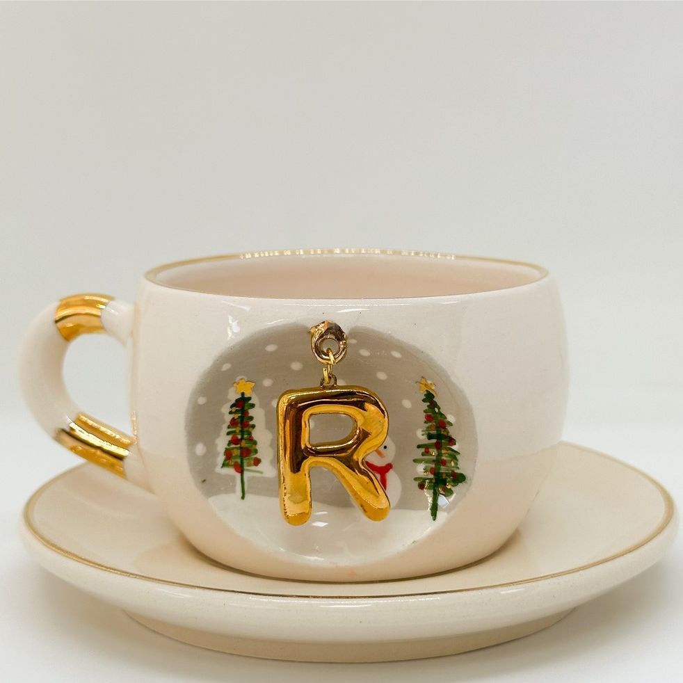 Porcelain tea cup and saucer with gold handle, hanging winter letter charm, evergreen trees