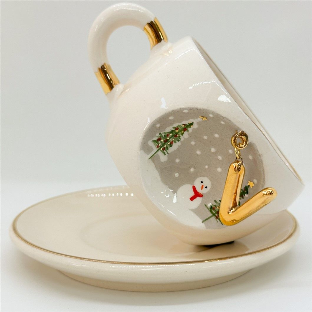 White porcelain tea cup tilted on saucer, gold letter, trees and snowman motif, 160 ml.