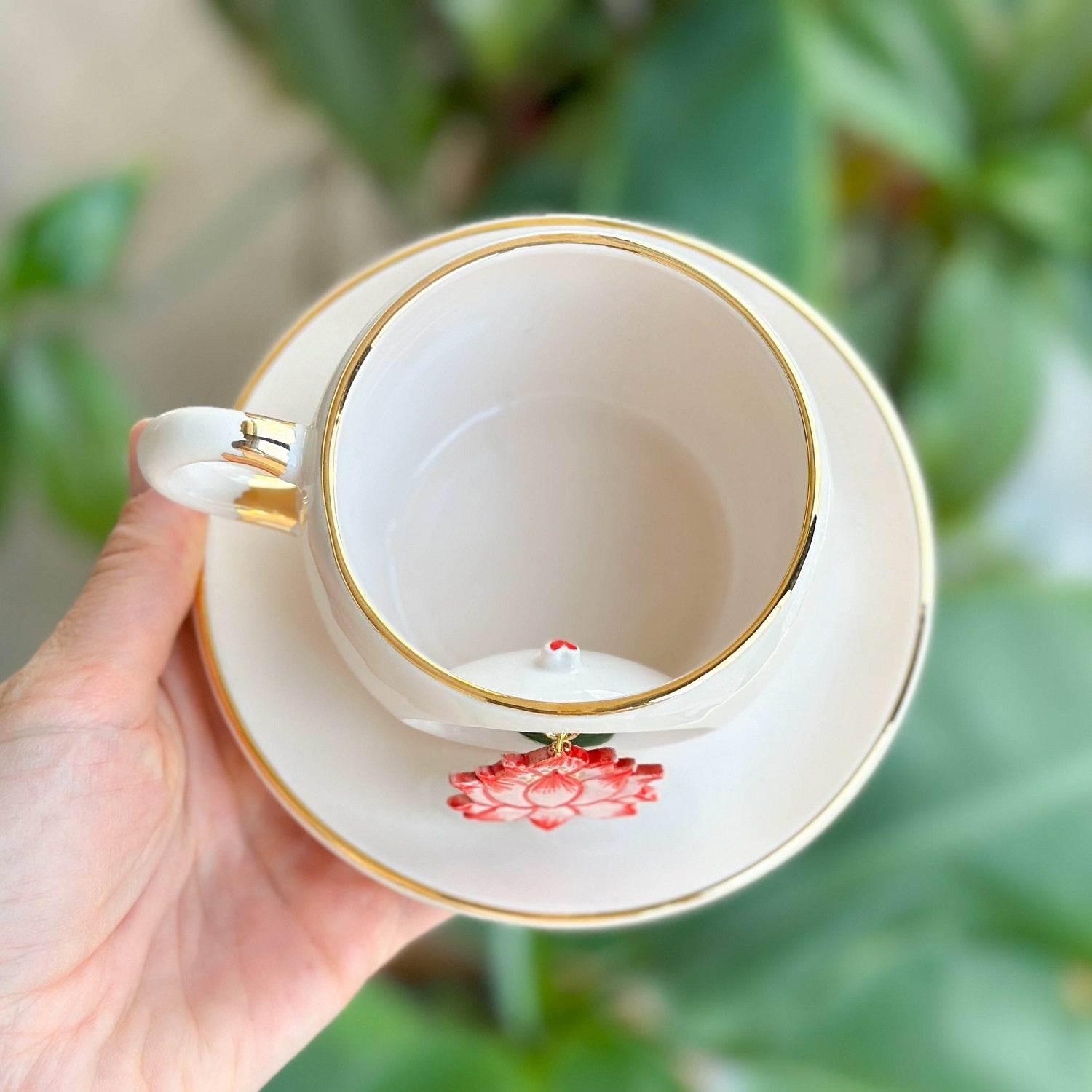 White mug with gold rim and red lotus flower on saucer, viewed from above