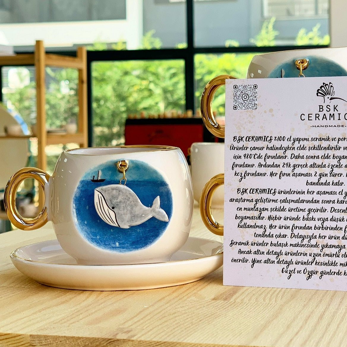 Ceramic coffee cup and saucer with blue whale illustration, gold handle and rim.