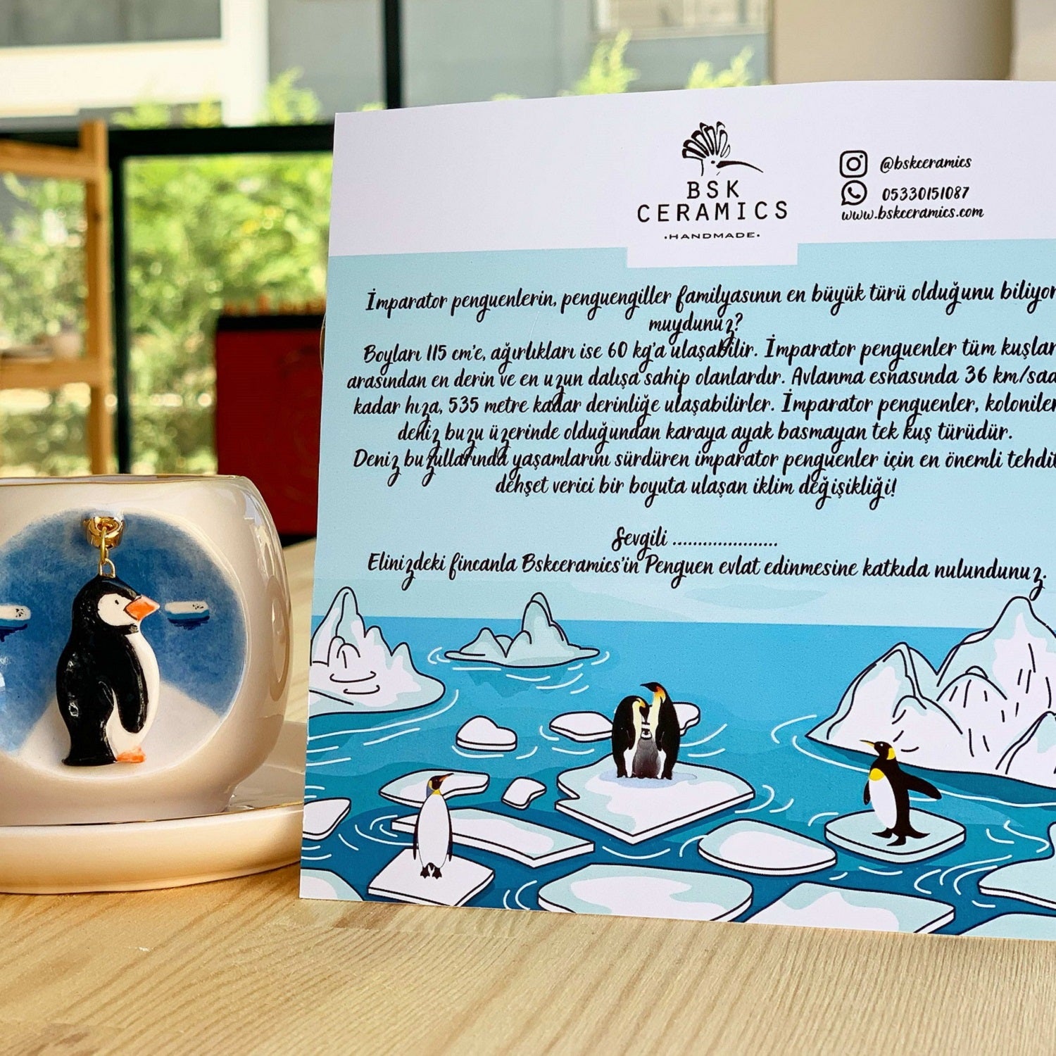 Ceramic coffee cup with penguin design and gold handle, on white saucer