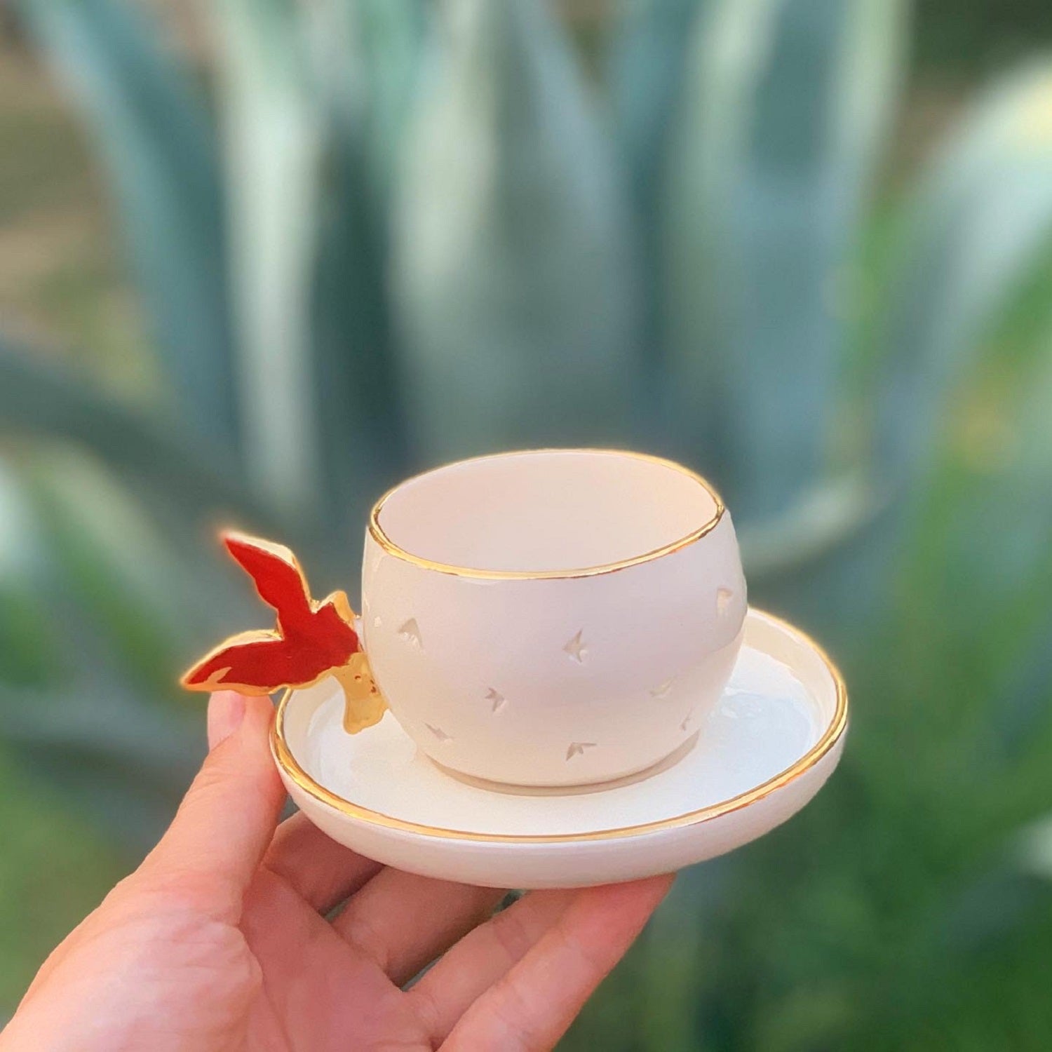 Transparent cup with gold rim and bird-shaped handle, on matching saucer