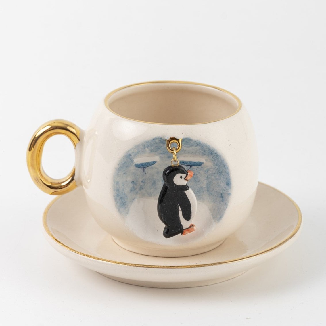 Ceramic coffee cup and saucer with penguin charm in blue splash print, gold handle