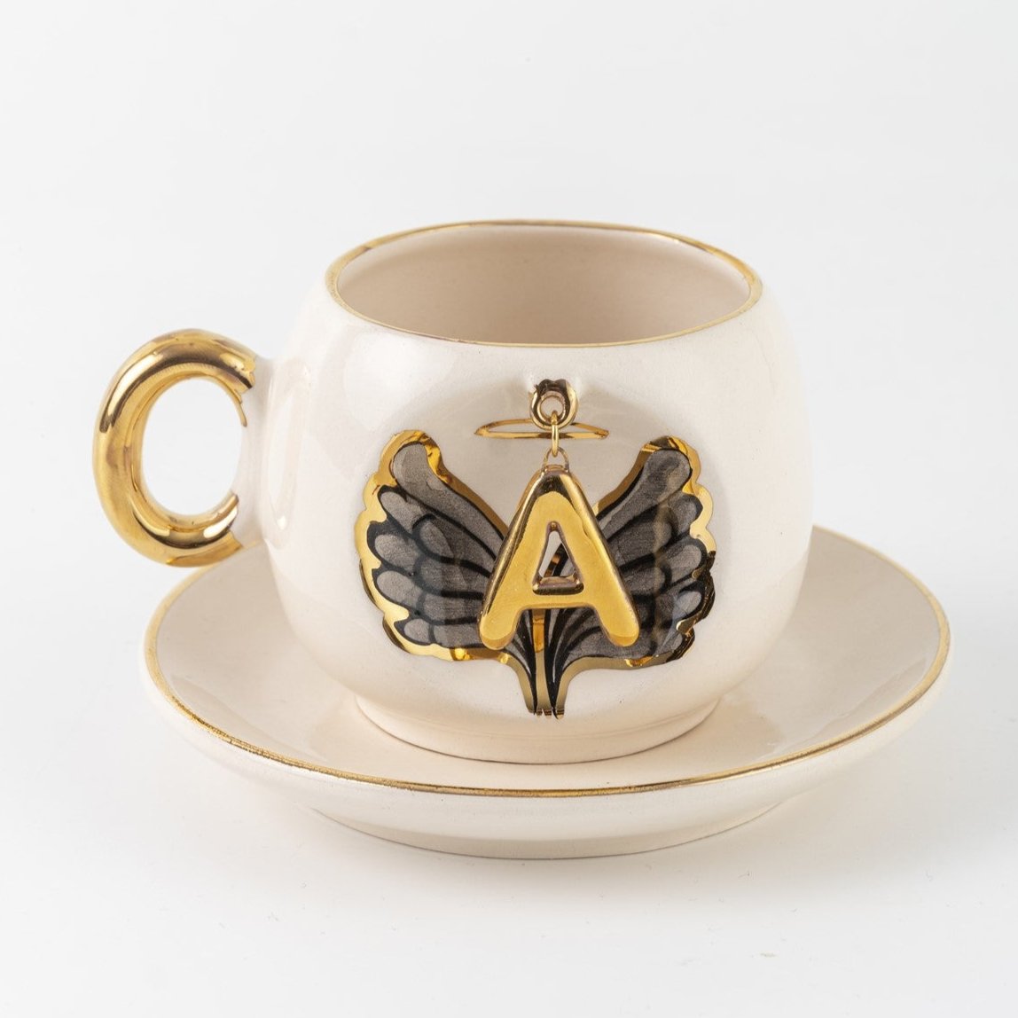 Porcelain cup and saucer with gold trim, black angel wing motif, letter A