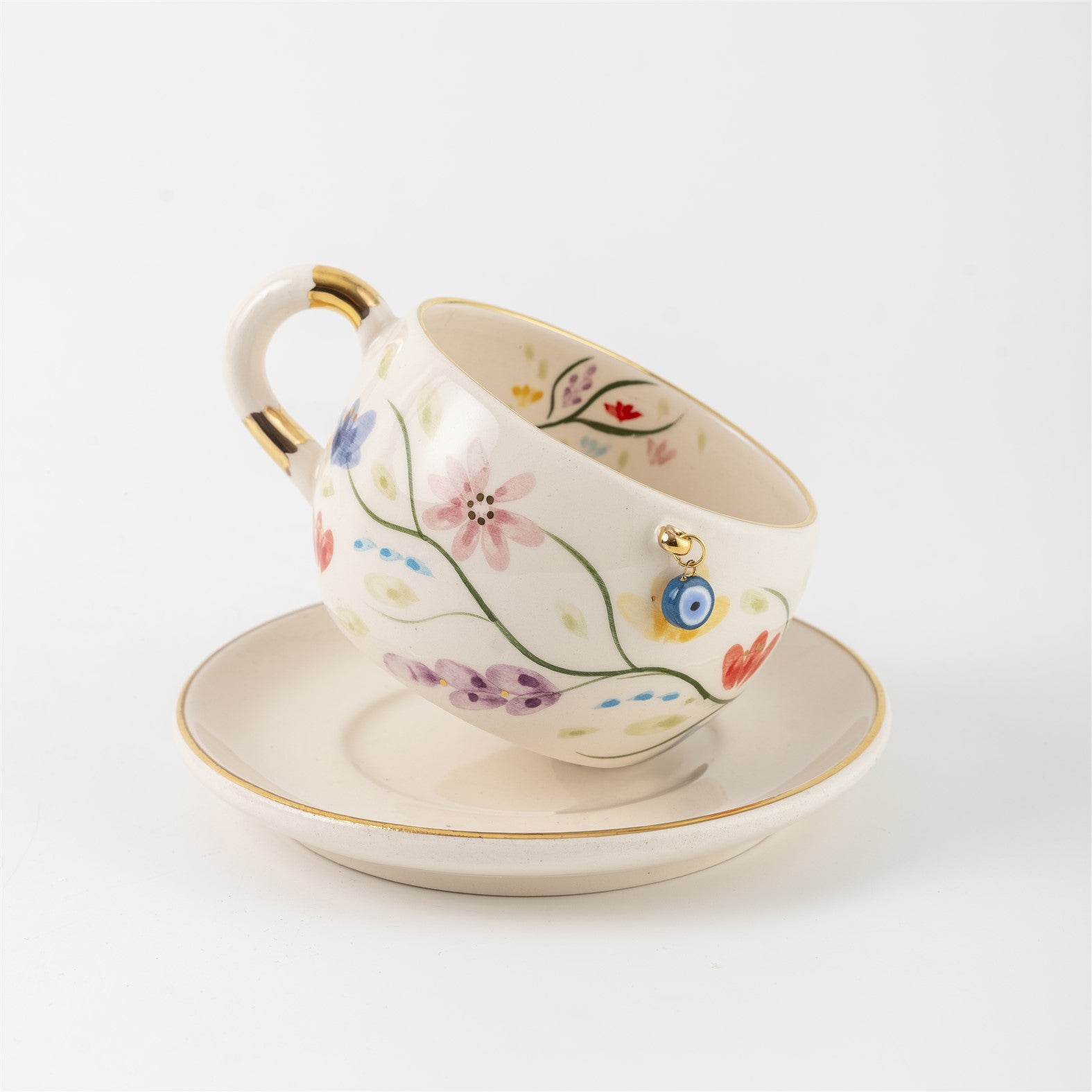Tea cup and saucer set with floral painting, blue eye detail, and gold handle