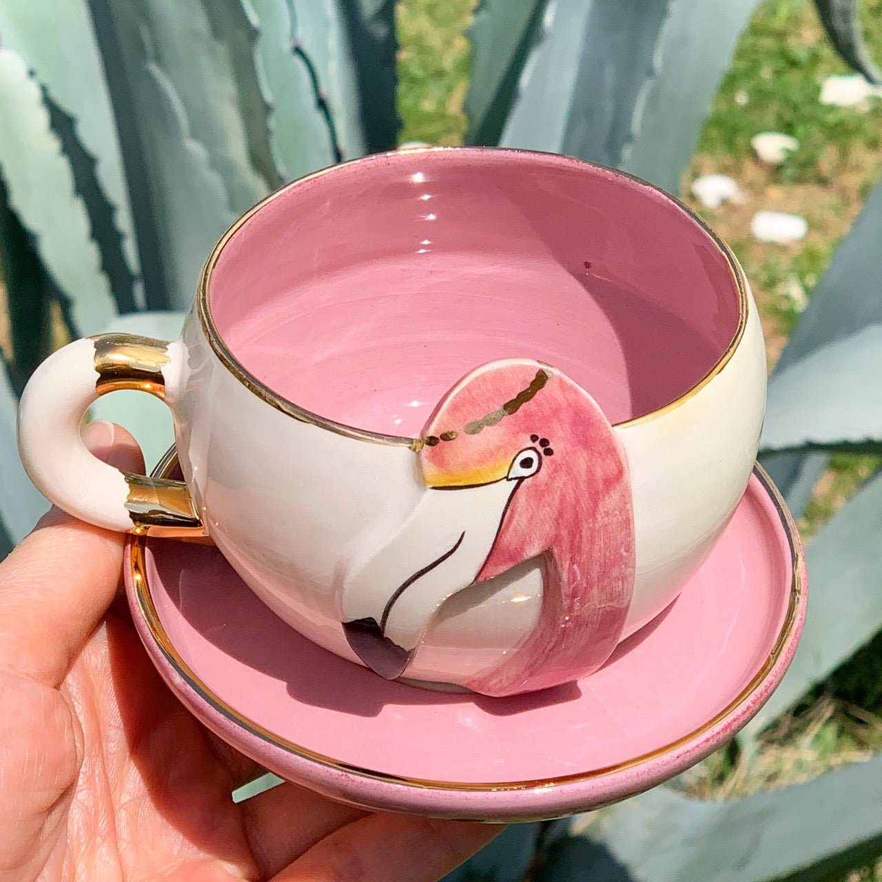 Pink tea mug with flamingo graphic and gold handle, shown with matching saucer