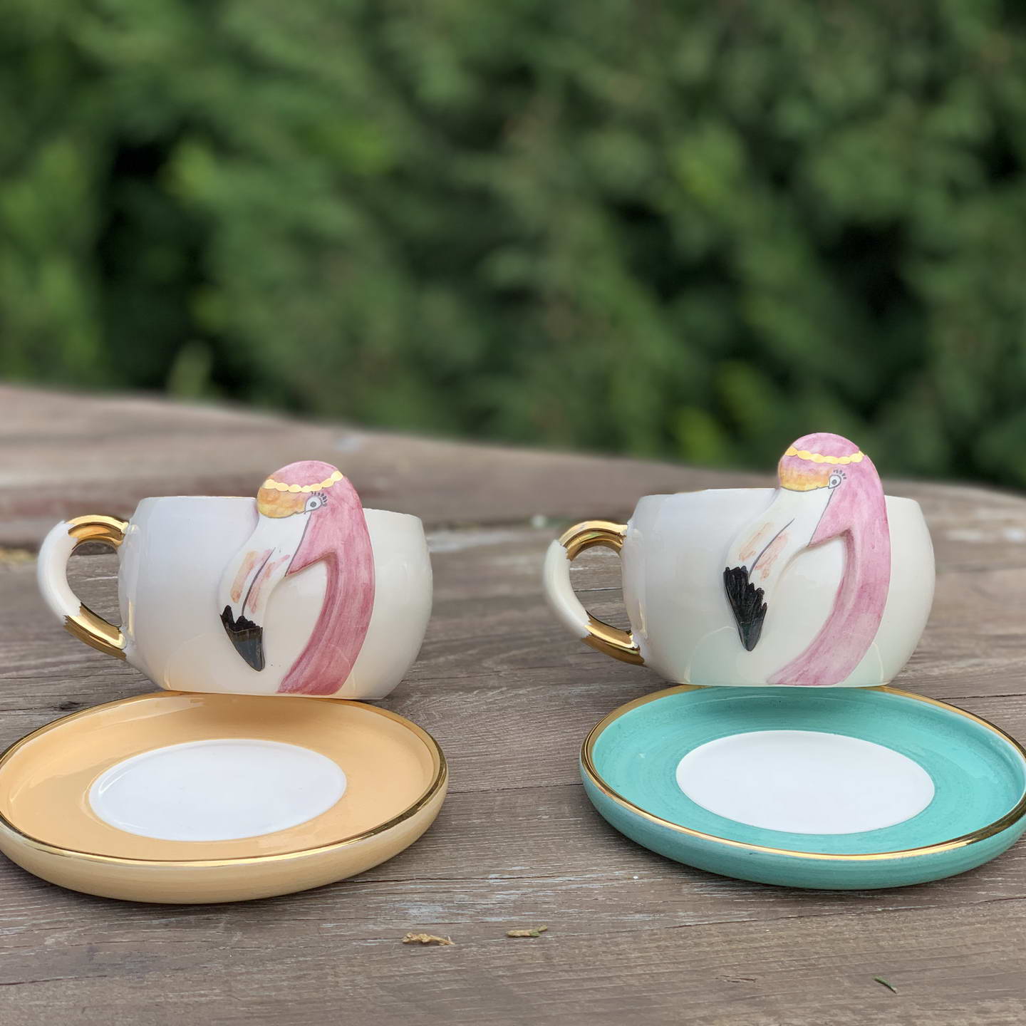 Two flamingo tea mugs on saucers, one Nile green with gold-tone handles