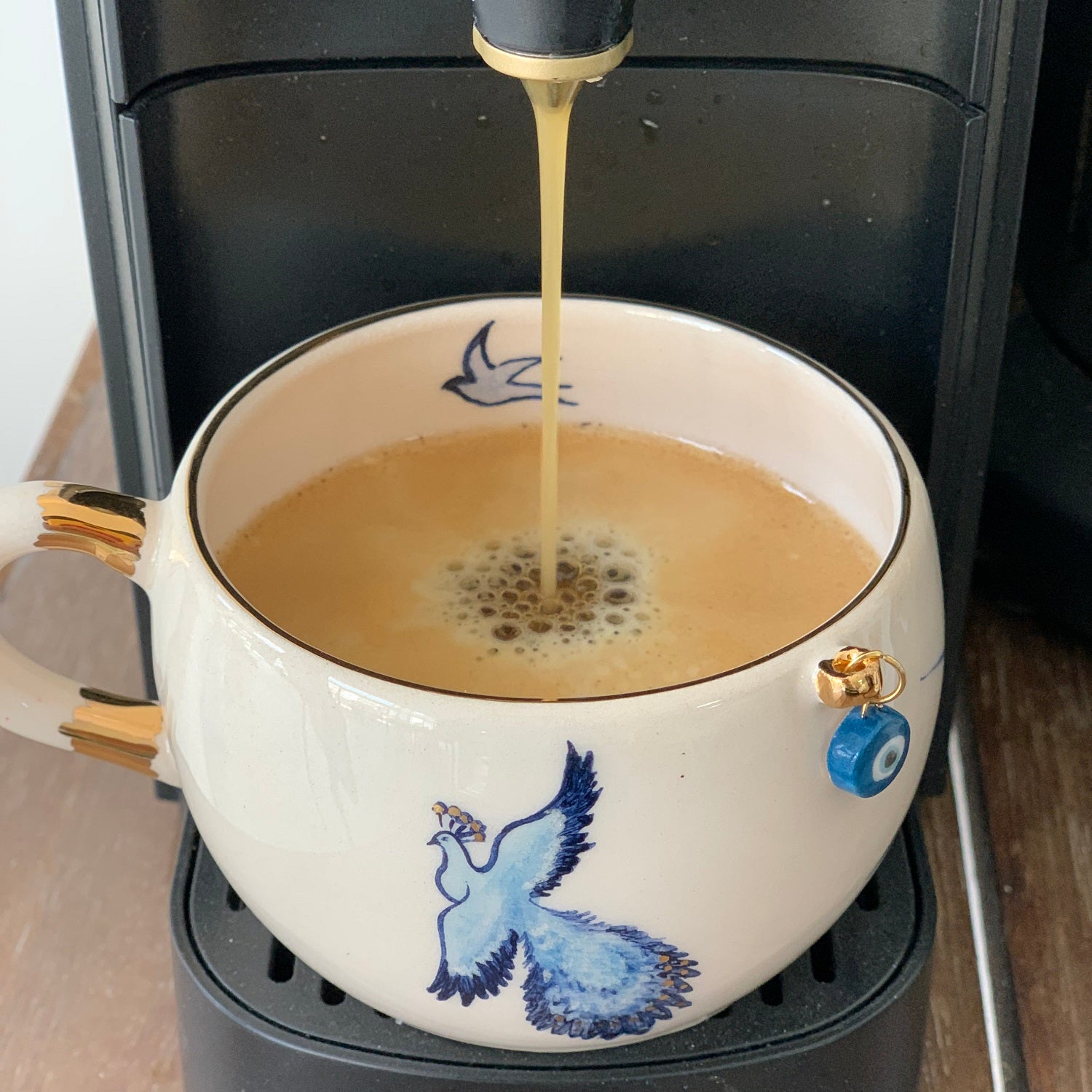Porcelain mug on a coffee maker with hot liquid and blue bird illustration