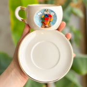 Cream ceramic mug base with gold rim, empty interior; balloon graphic on side