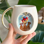 Ceramic mug with gold handle and rim, featuring a hot-air balloon dog illustration