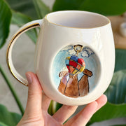Ceramic mug with gold handle and balloon-dog artwork, held in a hand