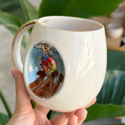 Ceramic mug with gold handle and side artwork of a hot-air balloon dog
