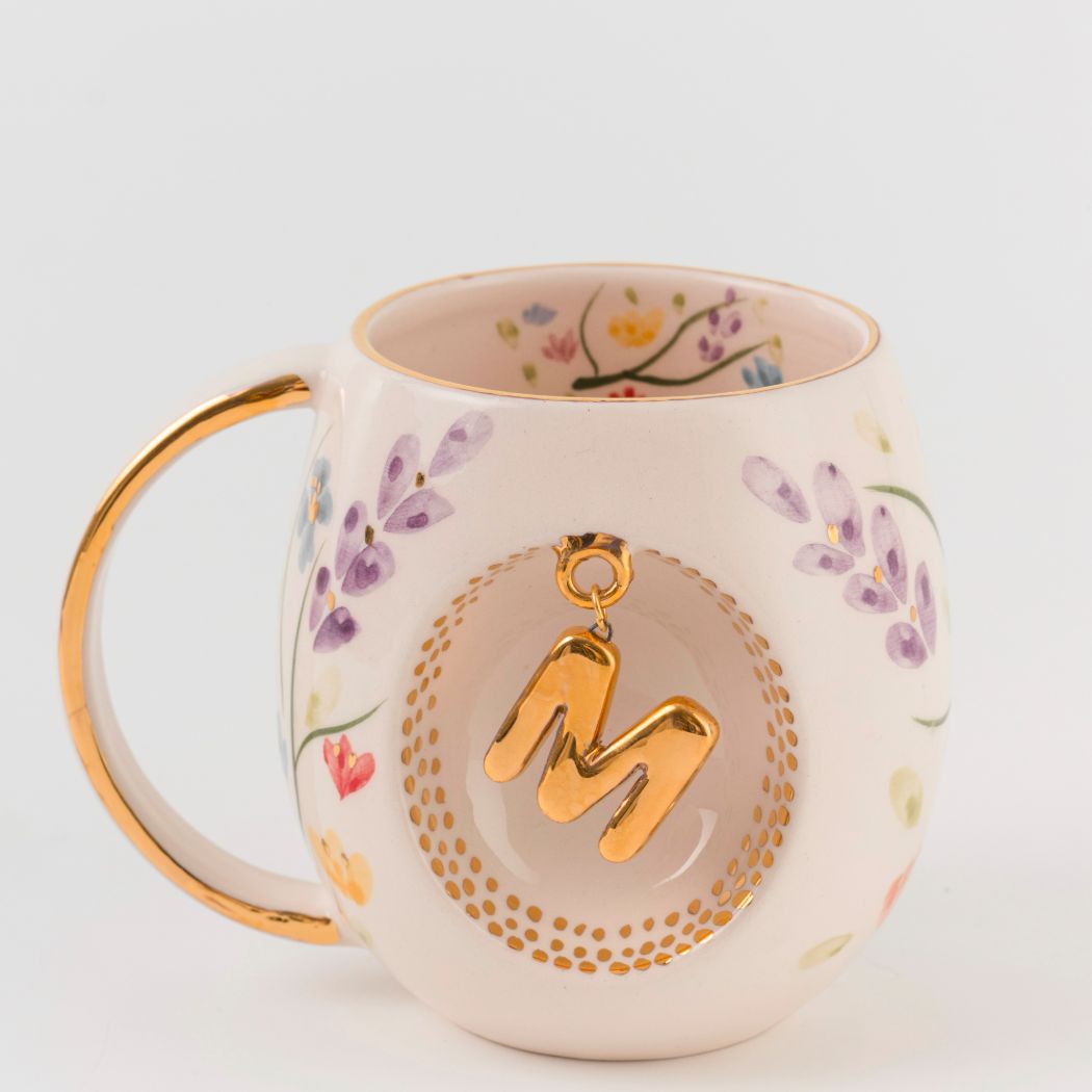 Porcelain mug with gold handle, floral pattern, and raised gold letter M on the front