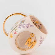 Porcelain mug with gold handle, floral pattern, and raised gold letter K in circular design