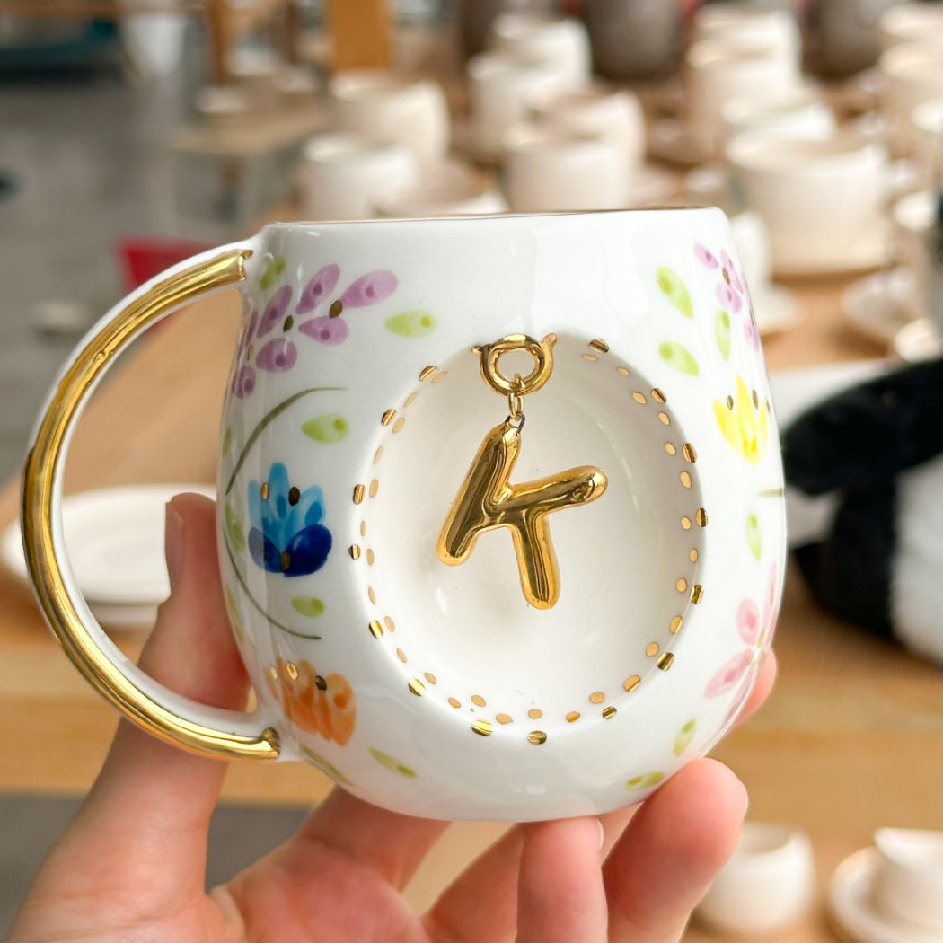 Porcelain mug with gold handle, floral pattern, and raised gold letter T on the front