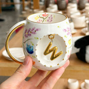 Porcelain letter mug with gold handle and spring floral design, featuring gold letter charm