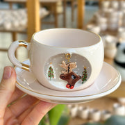 White mug and saucer with gold trim and inset reindeer illustration; gold-toned charm