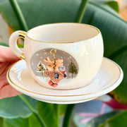 White deer mug with gold trim and reindeer and snowman graphic; matching saucer