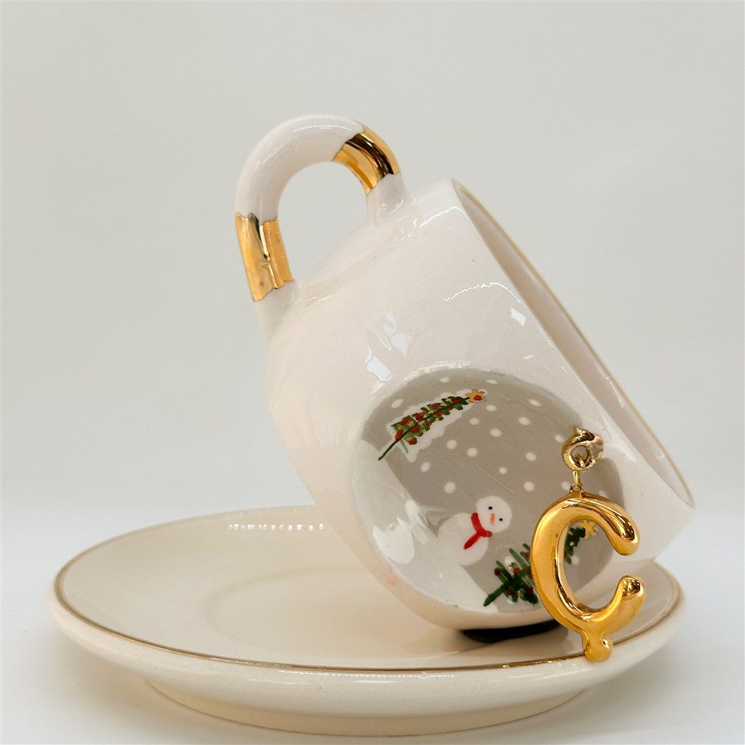 Porcelain tea cup and saucer, white with gold rim and handle; winter C letter and snowman
