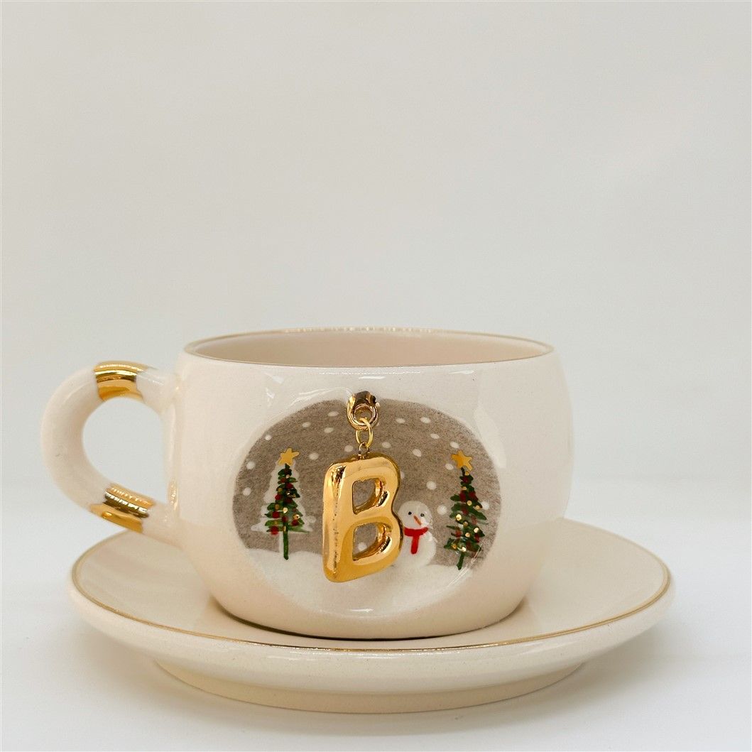 Porcelain tea cup and saucer, gold handle, letter D charm with tree and snow details