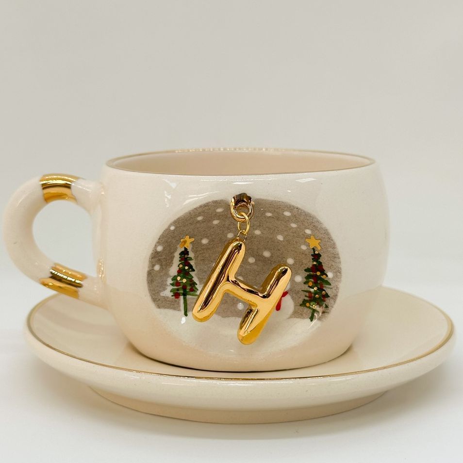 Porcelain tea cup and saucer set, white with gold letter charm, stars, and Christmas trees