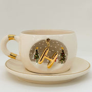 Porcelain tea cup and saucer set, white with gold letter charm, stars, and Christmas trees