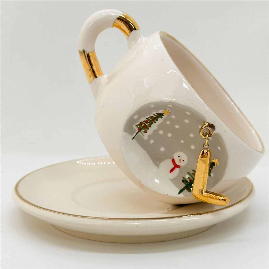 Porcelain tea cup with saucer, gold handle accents, winter letter charm with snowman and tree decor