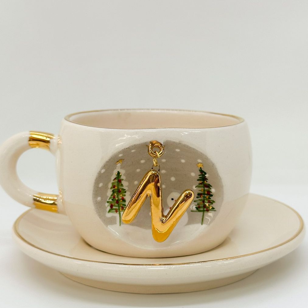 Porcelain tea cup with saucer, gold handle and winter letter charm with tree and speckle pattern