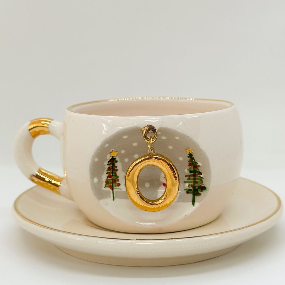 Porcelain tea cup and saucer with gold handle, hanging winter letter charm, evergreen trees
