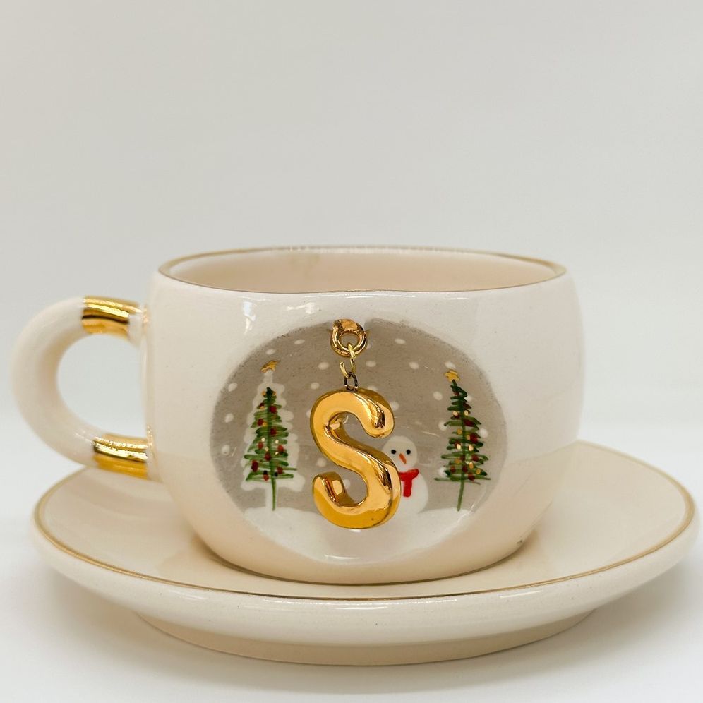 Porcelain tea cup and saucer with gold handle, hanging winter letter charm, snowman and trees