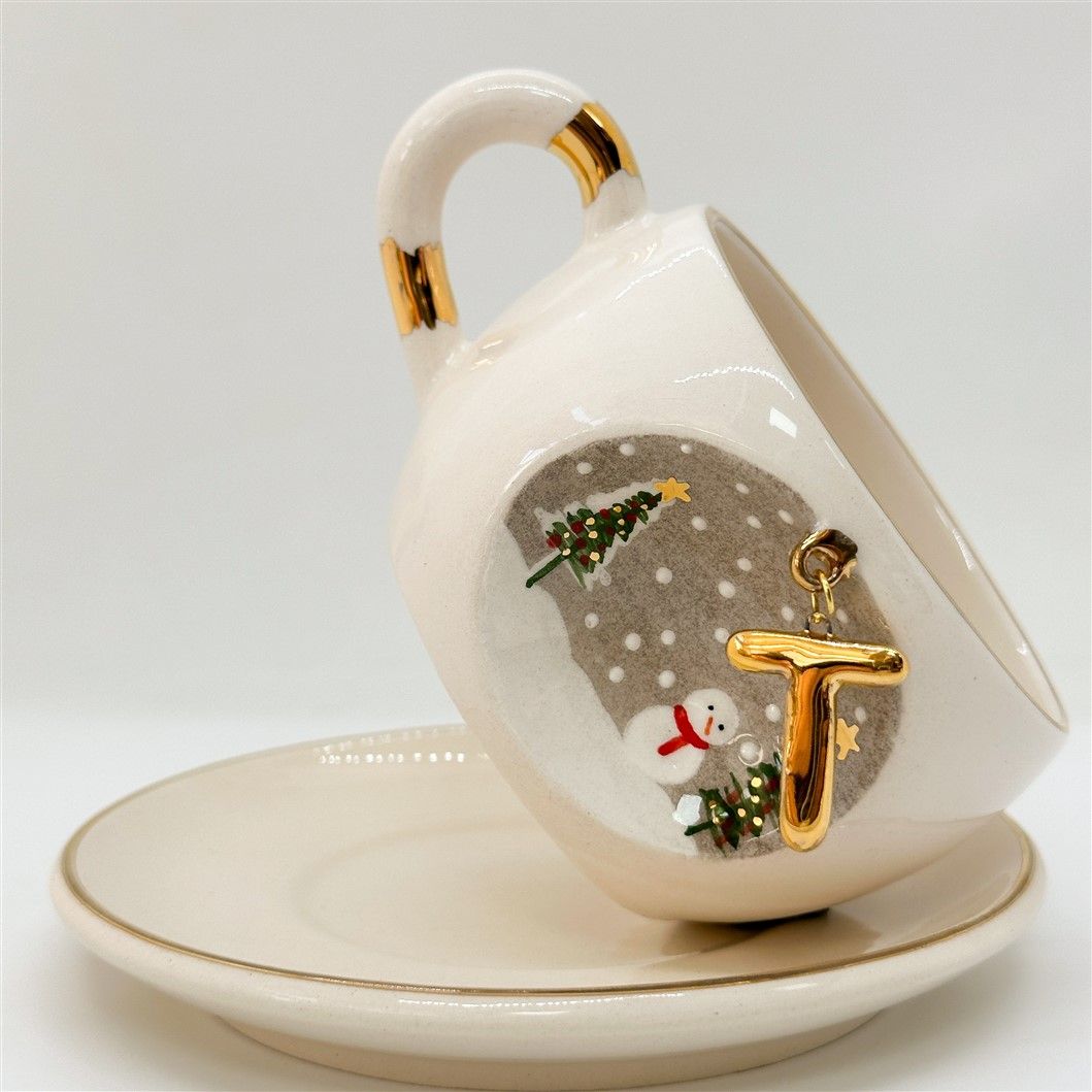 White porcelain tea cup with gold letter, trees and snowman graphic, on matching saucer, 160 ml.