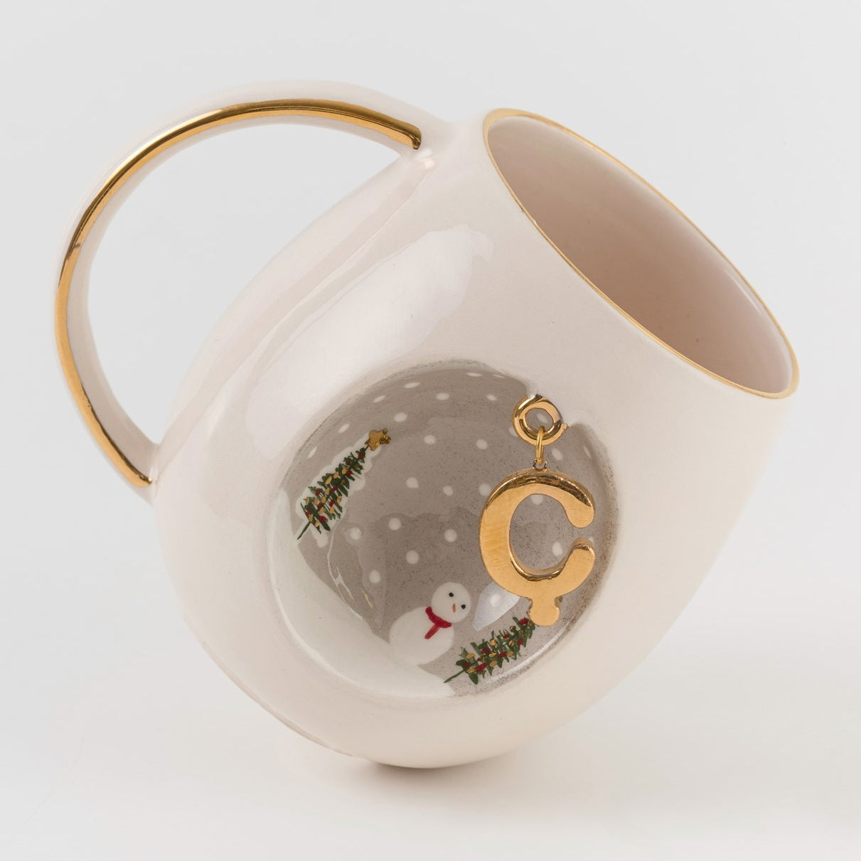 Porcelain mug angled view with gold-trim handle, C charm, winter trees and snowman