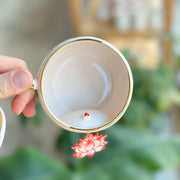 White mug with gold rim and red lotus flower detail inside, hand holding cup