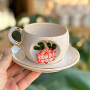 White mug and saucer with gold trim; red lotus and green leaves on cup