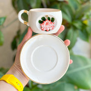 White mug with red lotus design and gold accents; cup held with saucer