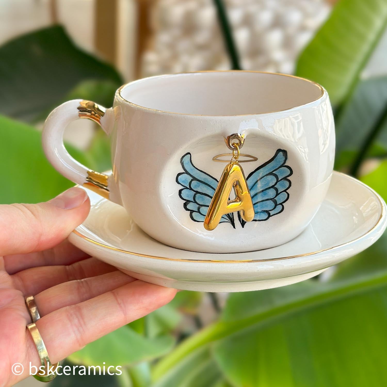 Ceramic angel-wing letter mug with blue wings and gold A, on matching saucer
