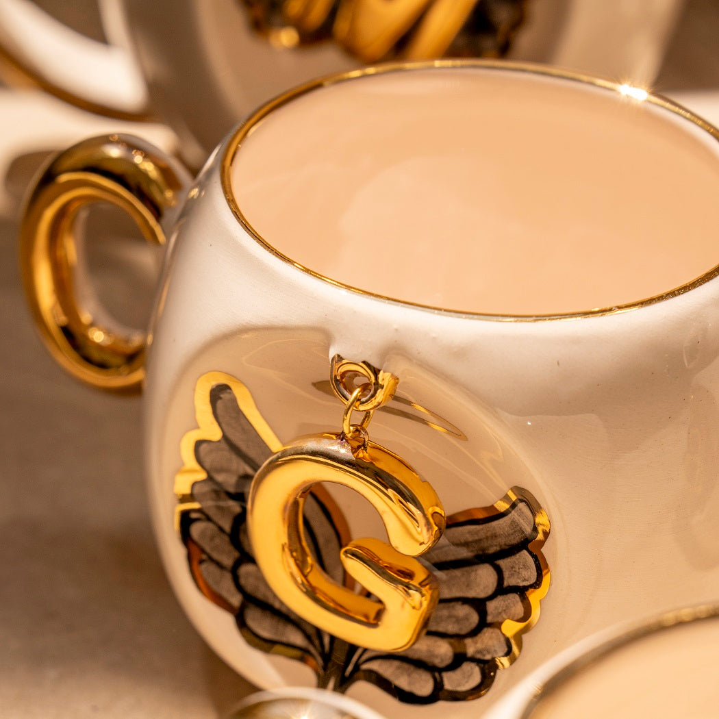 Porcelain cup detail with gold handle and angel wing emblem, letter C close-up