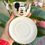 White ceramic tea mug with Mickey Mouse face, gold-edged saucer bottom