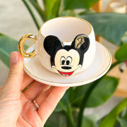 White coffee cup and saucer with Mickey Mouse graphic and gold handle