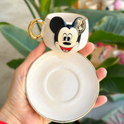 White coffee cup with Mickey Mouse face, gold rim, matching saucer